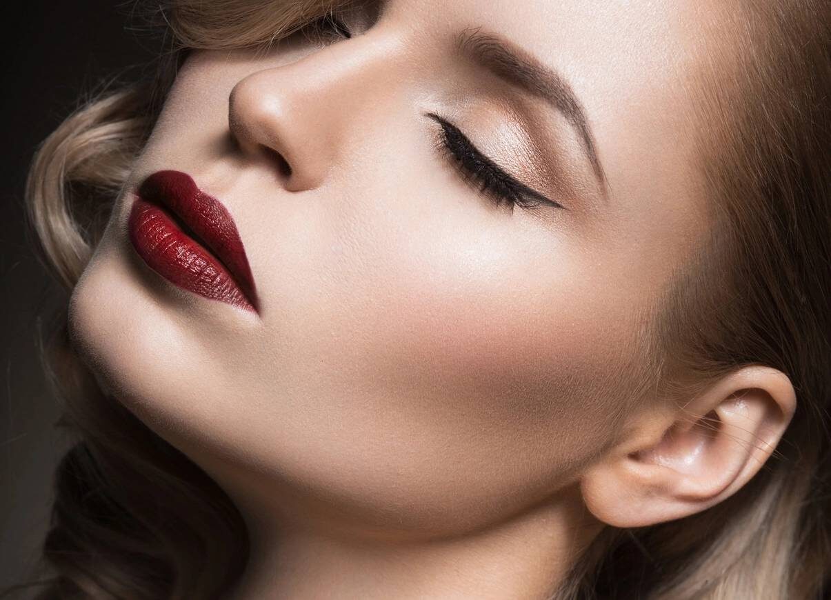 Close-up of a woman with flawless makeup, featuring bold red lips, defined eyeliner, and a soft blush highlighting her cheekbones, showcasing elegant beauty